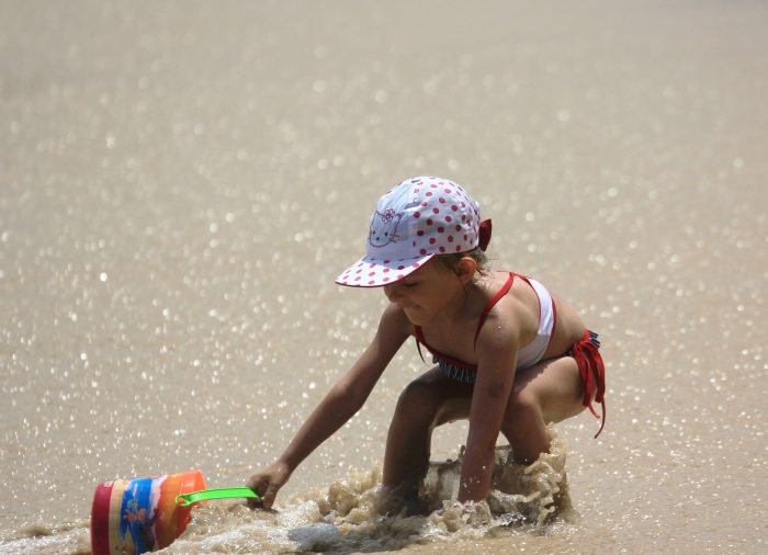 niña con gorrito jugando en la playa con balde