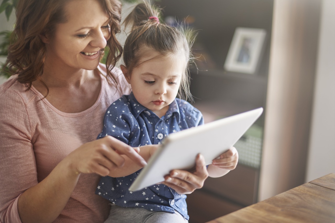 Madre sonríe con hija miran tablet