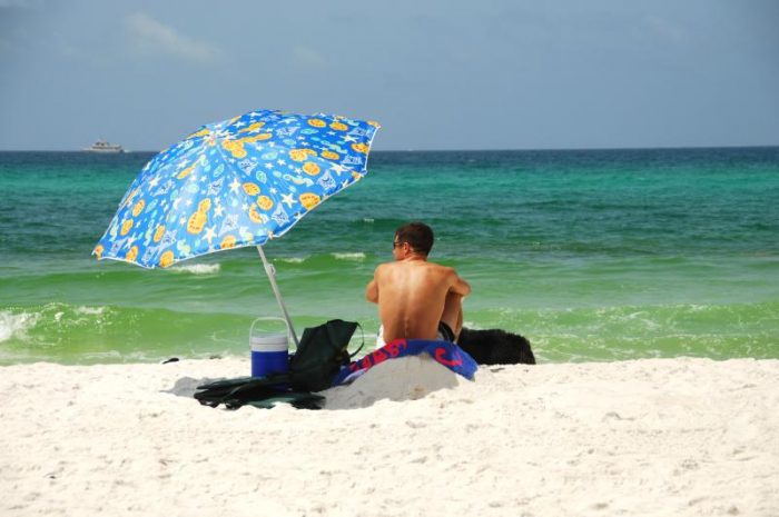 hombre en la playa en traje de baño junto a sombrilla