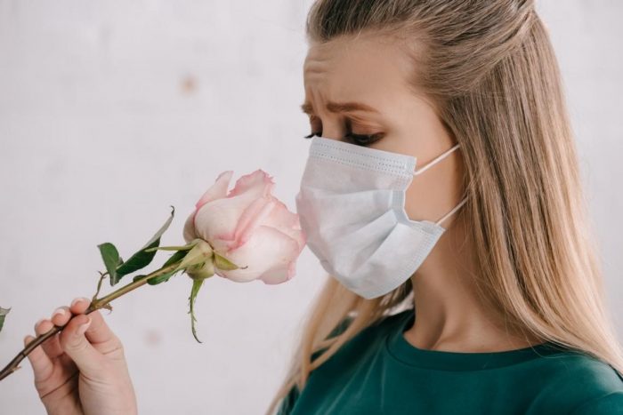 mujer con barbijo oliendo una flor